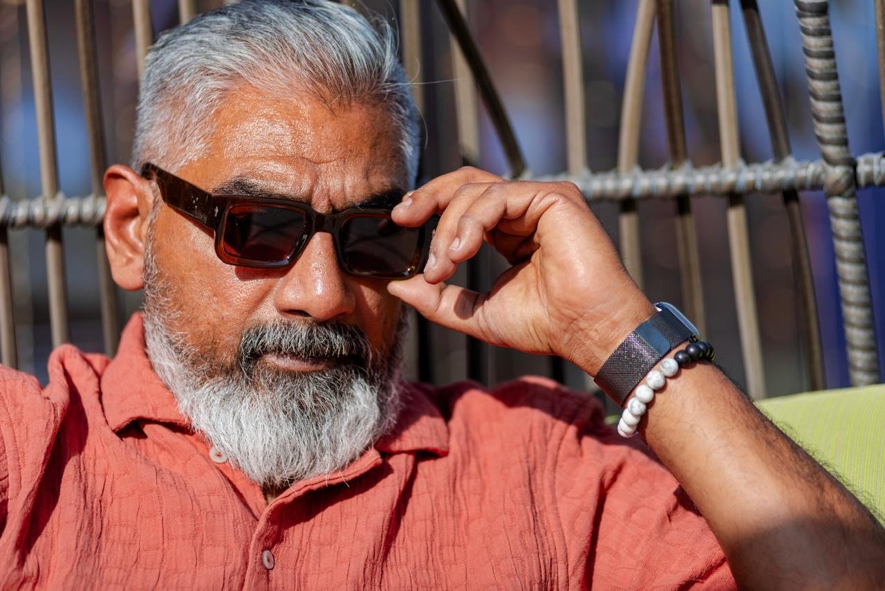 Sunlit close portrait of Dinesh wearing sunglasses and a coral shirt