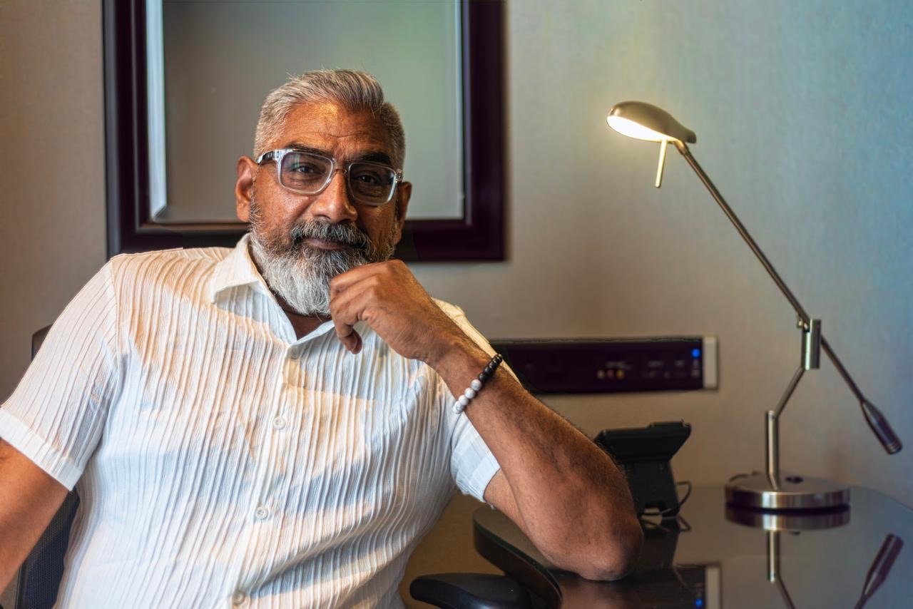 Dinesh seated at a desk in a white shirt, professional portrait